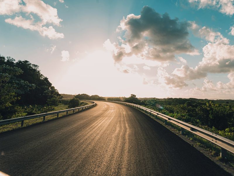 Carretera con curva y baranda, iluminada por el sol.